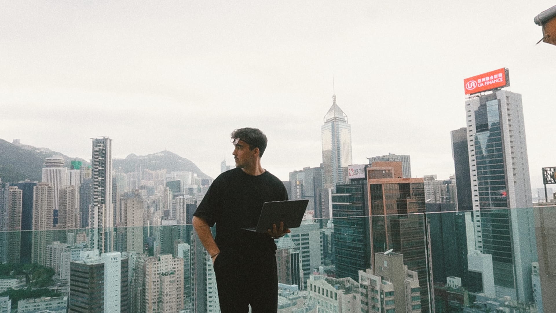 Yan Deschênes sur un toit-terrasse, ordinateur portable en main, devant les gratte-ciel de Hong Kong